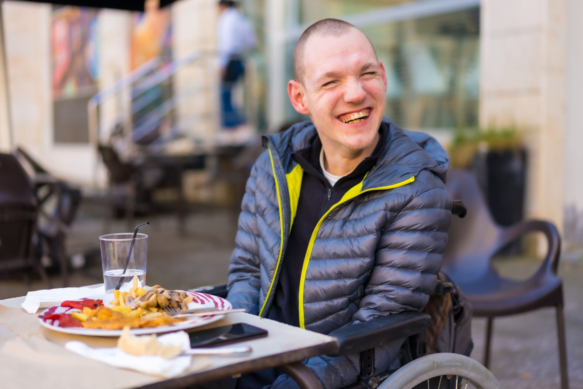 A cheerful young man in a wheelchair enjoying his meal outdoors on a sunny day